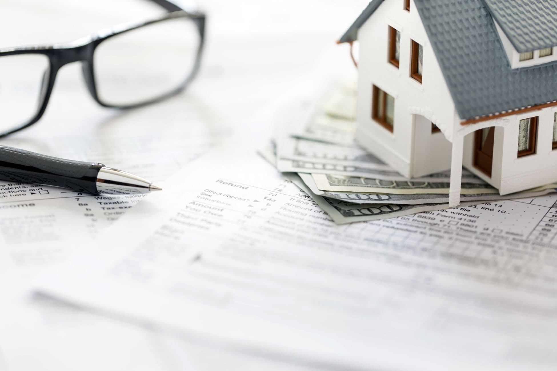 Model house placed on top of money and sheets of financial papers