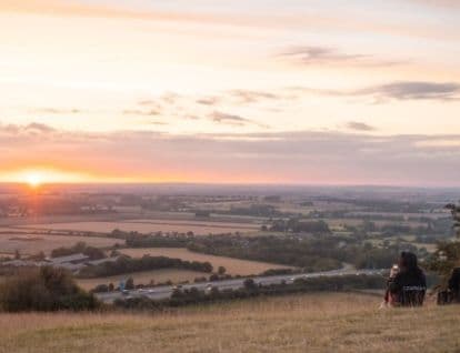 Sun setting in the distance overlooking fields and a motorway below