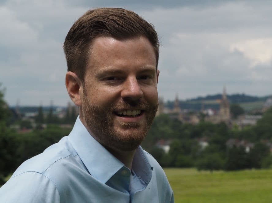 Grey Thompas smiling whilst stood in nature and the city in the background